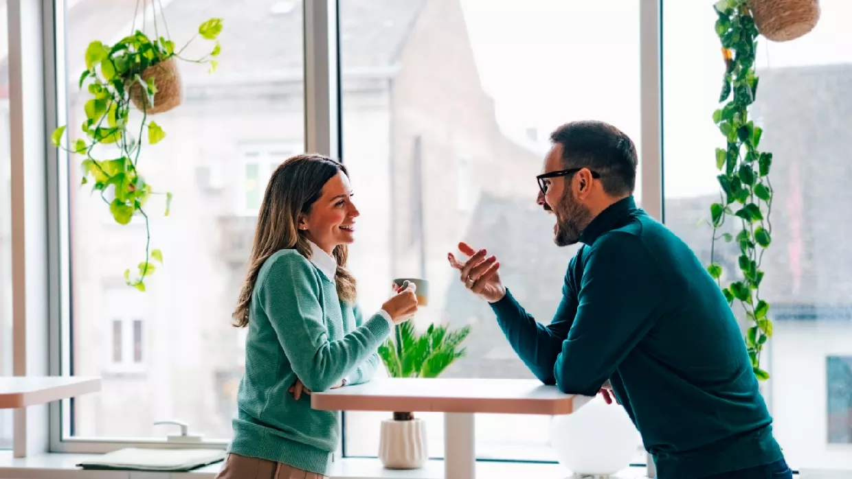 two colleagues, a man and a woman leaning over a tall table chatting while having a coffee  