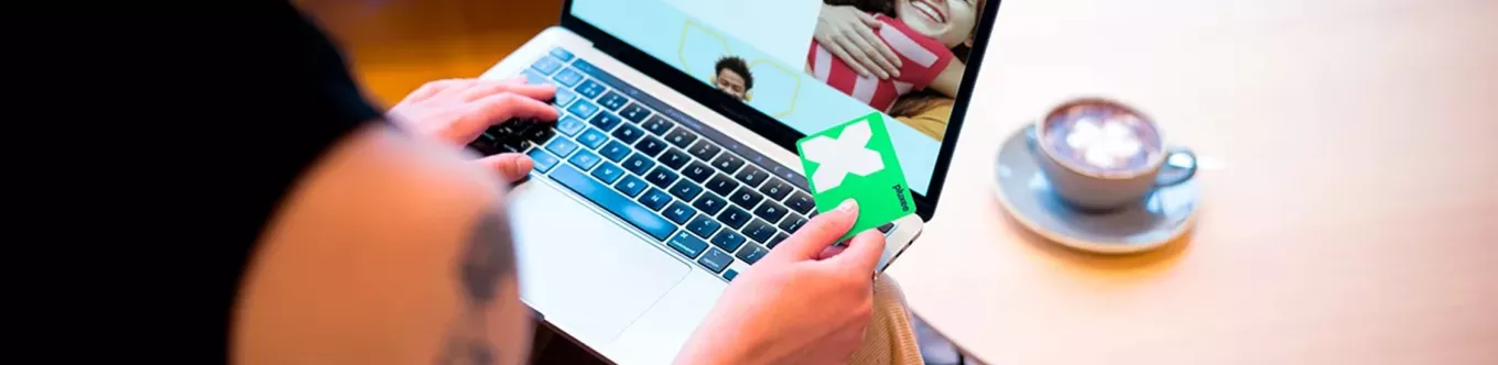 Femme assise devant un ordinateur portable, tenant une carte verte Pluxee tout en naviguant sur le site web de Pluxee, indiquant qu'elle explore les avantages de la carte en ligne. 