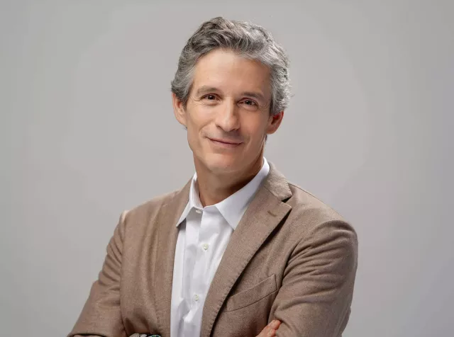 Headshot of Guillaume Boutin, grey hair in brown blazer smiling at camera