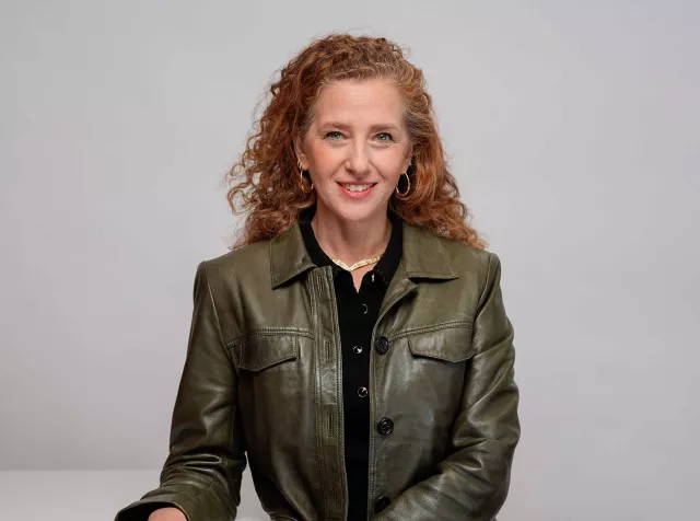 headshot of Cecilia de Pierrebourg, red curly hair and green leather jacket smiling at camera