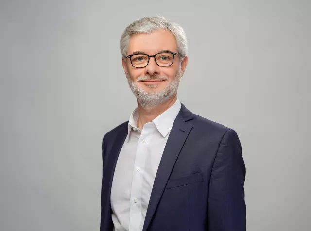 headshot of Jean Istasse, grey hair and glasses wearing blue blazer smiling at camera