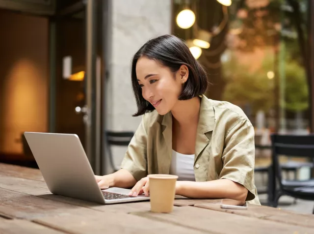 woman with short black hair sitting on a patio table with laptop working