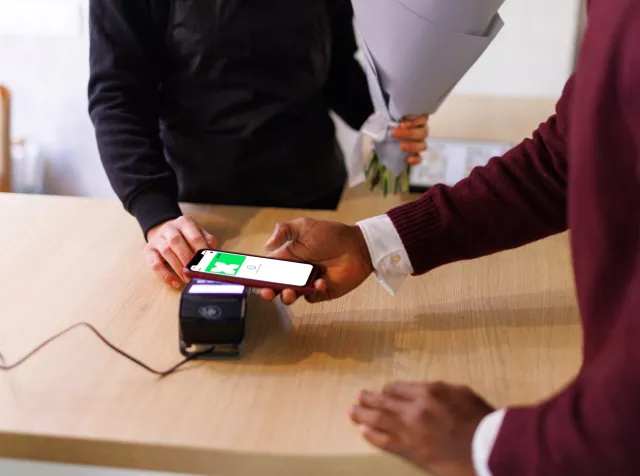 Man tapping cell phone on payment terminal with pluxee card displayed on phone screen