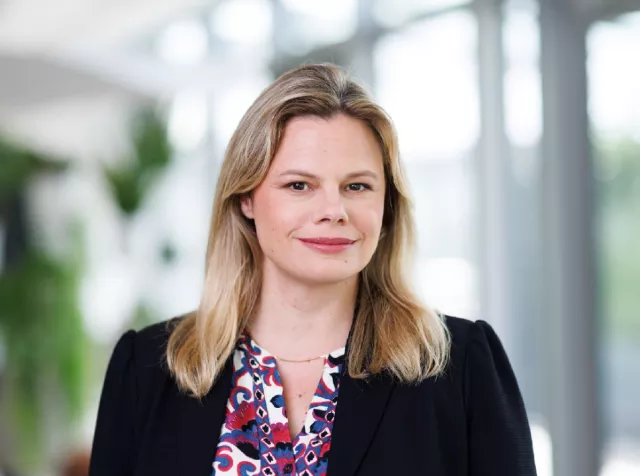 Headshot of Malena Gufflet, a white woman with blonde hair in a black blazer with purple and red patterned shirt, smiling at the camera 