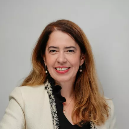 Headshot of middle aged woman with long brown hair smiling at camera in a white blazer 