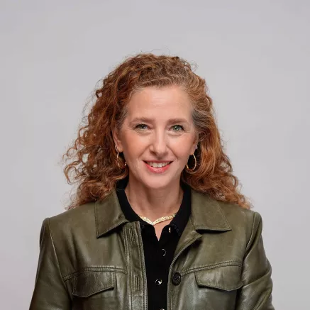 headshot of Cecilia de Pierrebourg, red curly hair and green leather jacket smiling at camera