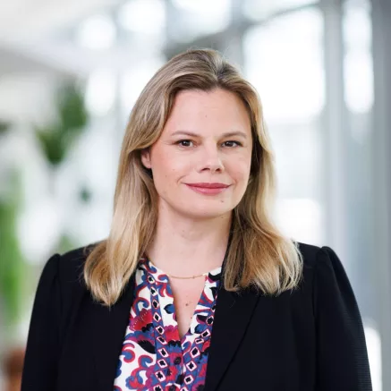 Headshot of Malena Gufflet, a white woman with blonde hair in a black blazer with purple and red patterned shirt, smiling at the camera 