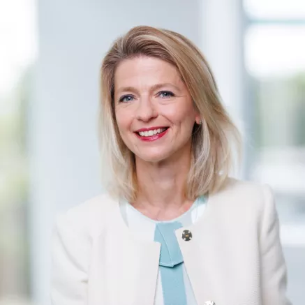 Headshot Viktoria Otero del Val, woman with short blond hair wearing red lipstick, a white blazer and light blue shirt 